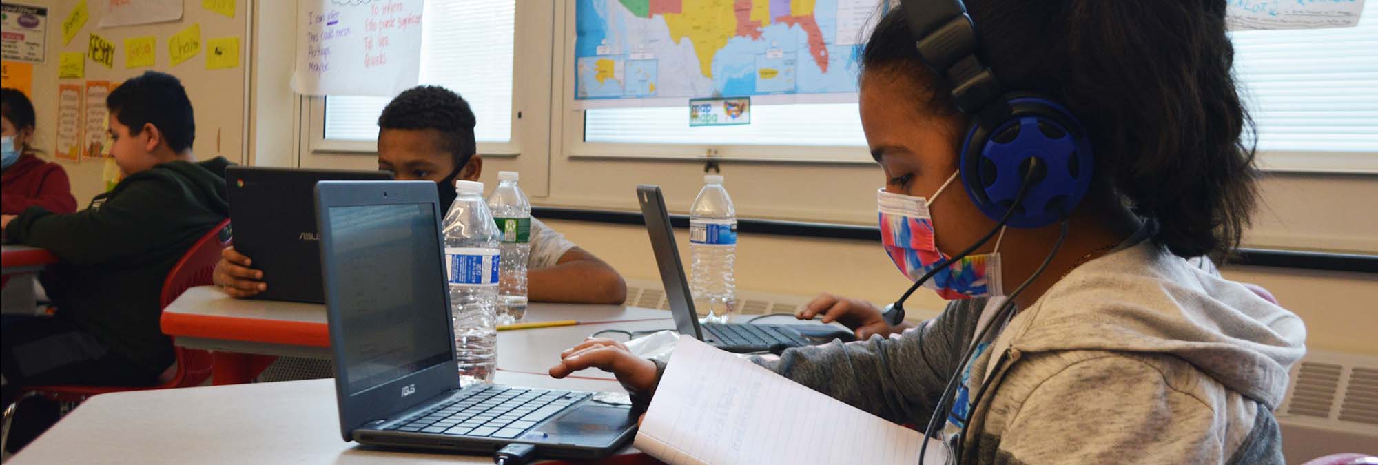 Student wearing headphones works on laptop in classroom